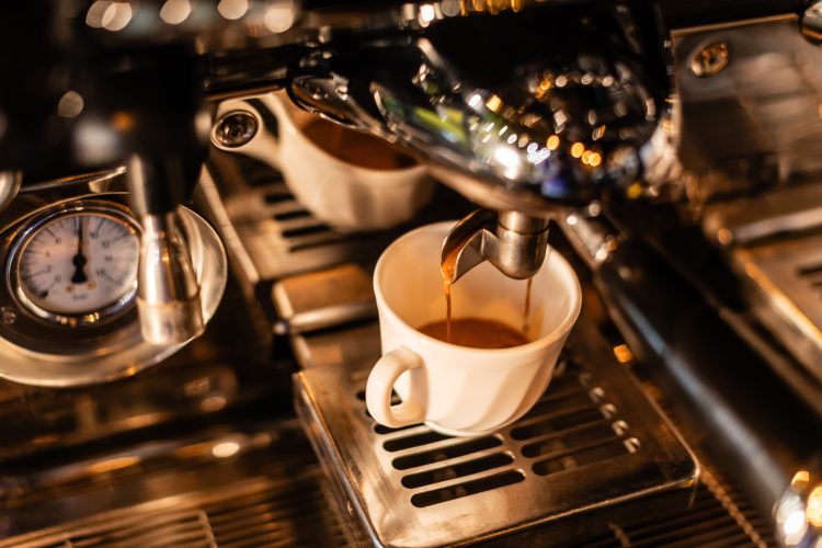 high angle view of coffee pouring in white cup from coffee machine in sunlight in cafe